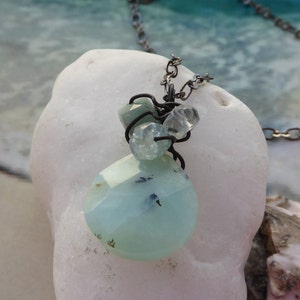 May include: A silver chain necklace with a light blue and clear gemstone pendant. The pendant is made of several small stones wrapped in wire.
