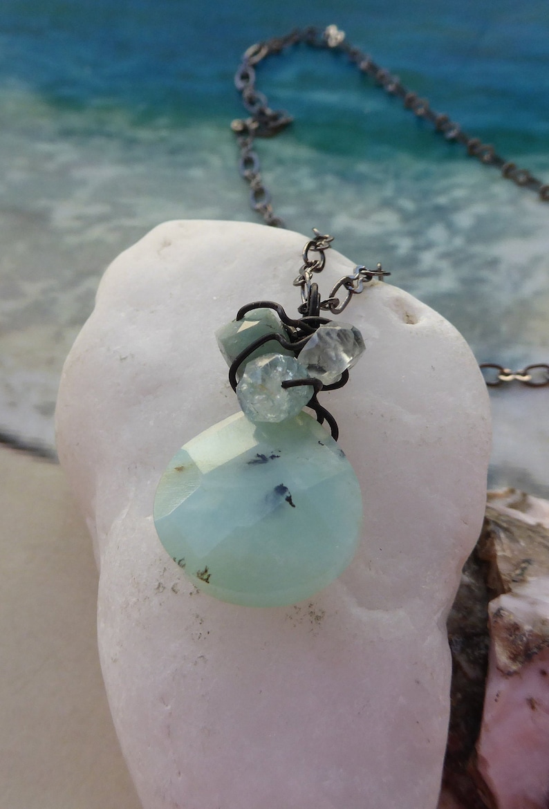 May include: A silver chain necklace with a light blue and clear gemstone pendant. The pendant is made of several small stones wrapped in wire.