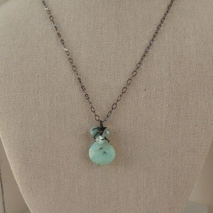 May include: A silver chain necklace with a light blue and green gemstone pendant. The pendant is made of multiple stones and is wrapped in silver wire.