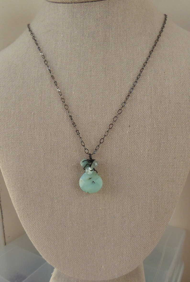 May include: A silver chain necklace with a light blue and green gemstone pendant. The pendant is made of multiple stones and is wrapped in silver wire.