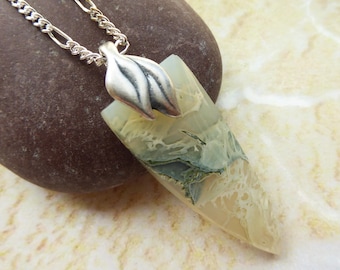 May include: A triangular pendant necklace featuring a polished stone with cream, tan, and sage green marbled patterns. The stone is held by a silver-toned metal bail with a leaf-like design, attached to a silver-toned metal chain with oval links.