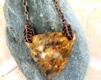 May include: A triangular pendant necklace featuring a mottled brown, tan, and cream-colored stone with a polished finish. The stone is held by two copper-toned metal leaf-shaped bails attached to a matching copper-toned chain with rectangular links.