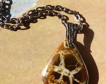 May include: A teardrop-shaped pendant featuring a polished brown stone with a network of light-colored, vein-like patterns. The stone is set in a silver-toned metal bail and hangs from a matching silver-toned chain with oval-shaped links.