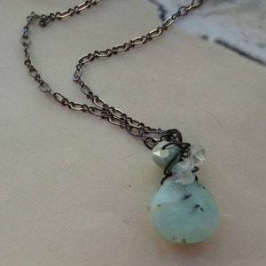 May include: A silver chain necklace with a light blue and white gemstone pendant. The pendant is made of a large, teardrop-shaped stone with smaller stones clustered around it.
