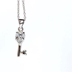 May include: A silver key pendant necklace with a clear crystal heart at the top. The key has a heart-shaped loop at the bottom.