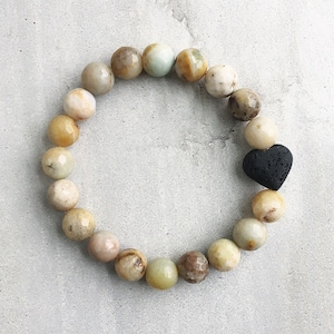 May include: A bracelet made of light green, brown, and white beads with a black lava rock heart charm.
