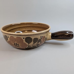 May include: A brown and beige ceramic bowl with a floral design and a brown handle. The bowl is ideal for serving soup, stew, or other dishes.