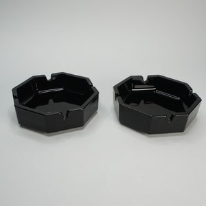 Peut inclure: Deux cendriers octogonaux en verre noir. Les cendriers sont en verre noir et ont une finition lisse et brillante.