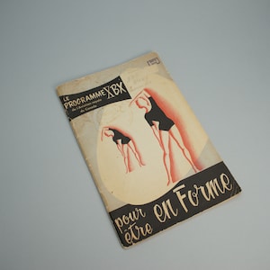 May include: A vintage book cover with a black and white illustration of two women in black swimsuits doing exercise poses. The cover is beige with red accents and the text "LE PROGRAMME XBX de l'Aviation royale du Canada pour etre en Forme" in black.