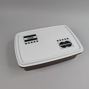 May include: A white plastic rectangular container with a brown lid. The container has a black and white Visa logo with five stars and a black and white Mastercard logo.