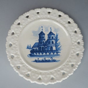 May include: A white ceramic plate with a blue and white design of a church with two towers. The plate has a scalloped edge with cutouts.