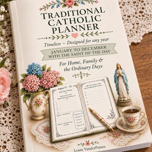 May include: A white book titled Traditional Catholic Planner with floral illustrations, a small statue of the Virgin Mary, a teacup, and an open planner page showing August 11-12. The cover features text including Timeless, Designed for any year, January to December with the Saint of the Day, For Home, Family & the Ordinary Days, and Leane VanderPutten.