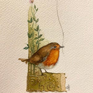 Könnte beinhalten: Ein Aquarellbild eines Rotkehlchens, das auf einem goldenen Zweig mit einer kleinen rosa Blume sitzt und an dem ein goldener herzförmiger Ballon mit einer Schnur befestigt ist.