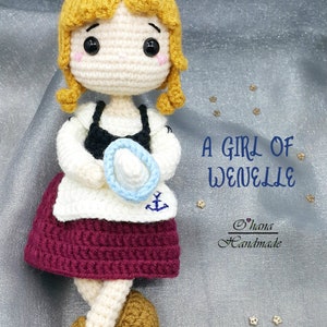 May include: A crocheted doll with blonde hair, wearing a white dress with a blue anchor, a burgundy skirt, and brown shoes. The doll is holding a blue and white hat. The text "A Girl of Wenelle" and "Ohana Handmade" is visible in the image.