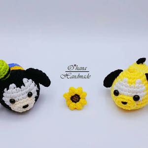 Puede incluir: Dos juguetes de peluche tejidos a crochet, un perro blanco y negro con un sombrero verde y un perro amarillo, y un girasol tejido a crochet amarillo.