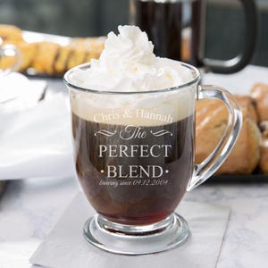 Może przedstawiać: Przezroczysty kubek ze szklanym uchwytem, wypełniony kawą i przykryty bitą śmietaną. Kubek jest grawerowany tekstem "Chris & Hannah The Perfect Blend. Brewing since 09.12.2009."