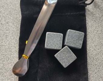 May include: A set of three gray stone whiskey chilling cubes in a black velvet pouch with a silver and gold metal tong.