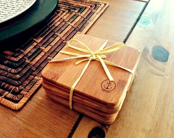 May include: Set of four natural bamboo coasters with a nautical anchor logo and a yellow ribbon tied around them.