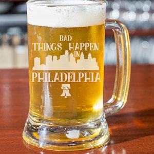 May include: A clear glass beer stein with a white design that reads "Bad Things Happen in Philadelphia" with a skyline and a Liberty Bell graphic.