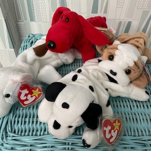 May include: Four plush dog toys in various colors and patterns. A red dog, a white dog with brown spots, a white dog with black spots, and a white and brown dog. Each dog has a heart-shaped tag.
