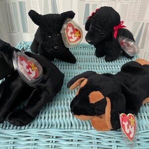 May include: Four plush dog toys in various poses. Three are solid black, and one is black and brown. Each toy has a Ty heart-shaped tag attached. One black dog has a red bow.