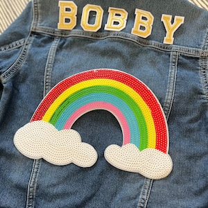 May include: A blue denim jacket with a rainbow and cloud patch and the name "BOBBY" in gold letters on the back.