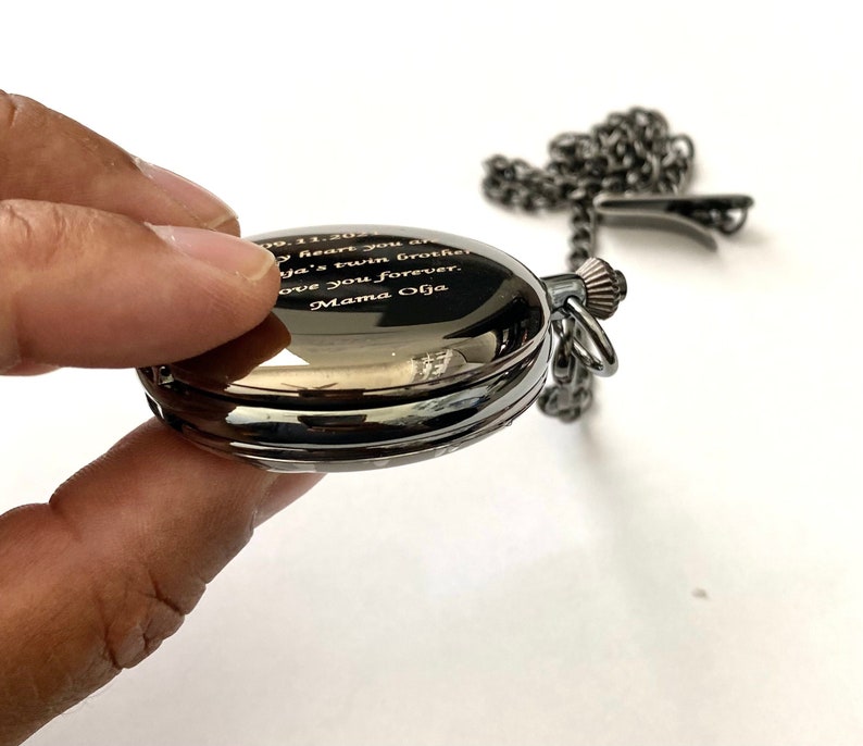May include: A black pocket watch with a silver chain. The watch face is engraved with the text "09.11.2021 My heart you are my twin brother Love you forever Mama Olga"