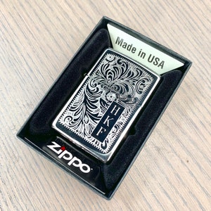 May include: A silver Zippo lighter with a black background and an intricate floral design. The lighter is engraved with the initials "HKF" and the words "Made in USA".