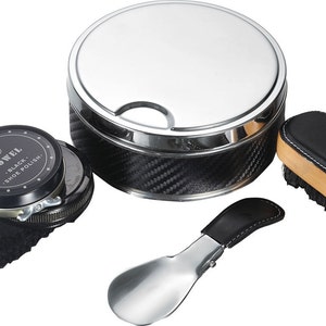 May include: A shoe care kit with a large, round, silver-colored container with a carbon fiber pattern, a shoe brush, shoe polish, a shoe horn, and a black cloth. The shoe polish tin reads "ROWEL BLACK SHOE POLISH."