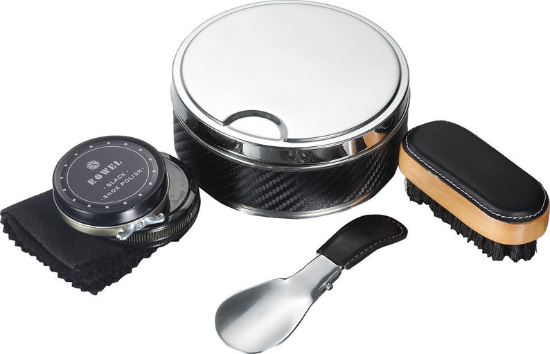 May include: A shoe care kit with a large, round, silver-colored container with a carbon fiber pattern, a shoe brush, shoe polish, a shoe horn, and a black cloth. The shoe polish tin reads "ROWEL BLACK SHOE POLISH."
