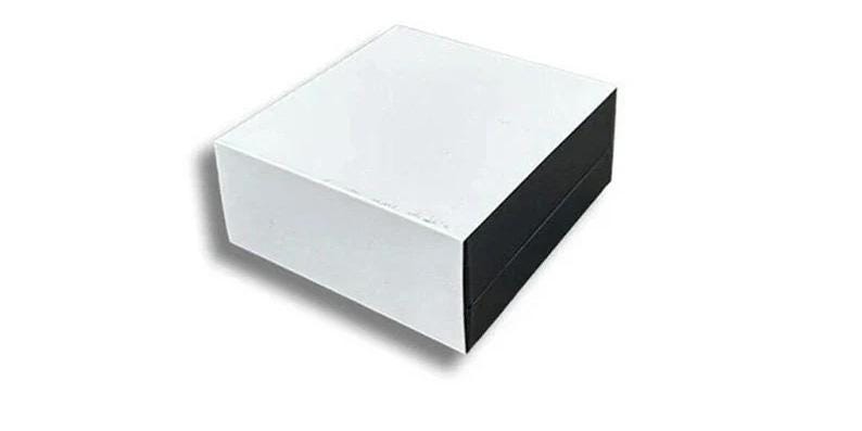 May include: A white square box with a black lid. The box is made of cardboard and has a smooth surface.