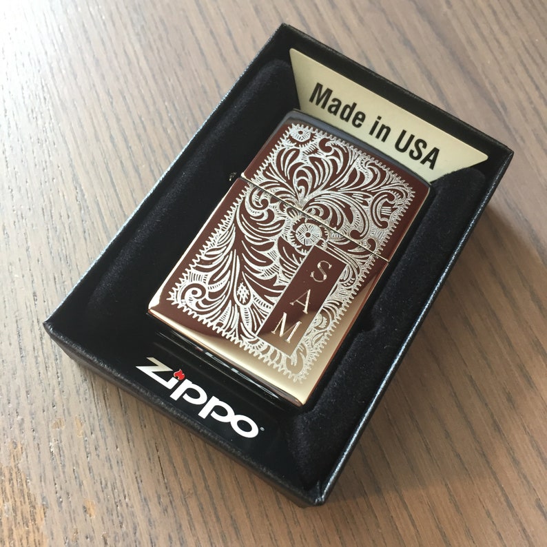 May include: A silver Zippo lighter with an engraved floral design and the initials "SAM" on the front. The lighter is in a black box with the words "Made in USA" and "Zippo" printed on it.
