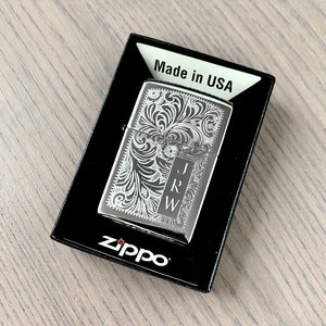May include: A silver Zippo lighter with an engraved floral design and the initials "J.R.W." on the front. The lighter is in its original box, which says "Made in USA" and has the Zippo logo.