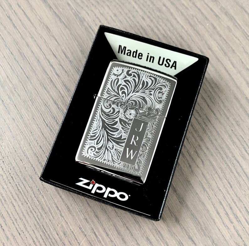 May include: A silver Zippo lighter with an engraved floral design and the initials "J.R.W." on the front. The lighter is in its original box, which says "Made in USA" and has the Zippo logo.