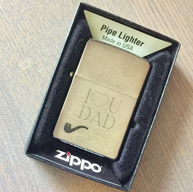 May include: A silver Zippo lighter in a black box with the words "Pipe Lighter Made in USA" on the box. The lighter has an engraved design that says "I &hearts; U DAD" with a pipe symbol.