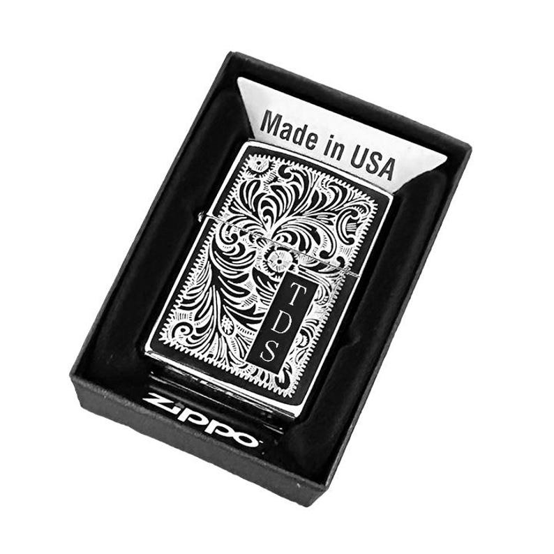 May include: A silver Zippo lighter with a black and white engraved design. The design features a floral pattern and the initials "TDS". The lighter is in a black box with the words "Made in USA" and "Zippo" printed on it.