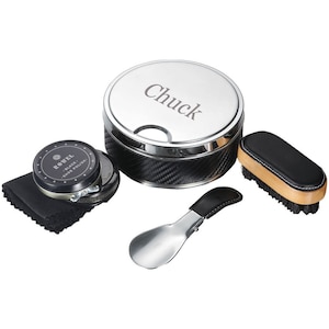 May include: A shoe shine kit with a silver lid engraved with "Chuck". The kit includes a black shoe brush, shoe polish, a black cloth, and a shoe horn. The container has a carbon fiber design.