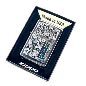 May include: Silver Zippo lighter with an engraved floral design and the initials "KAK" on the front. The lighter is in a black box with the words "Made in USA" and "Zippo" printed on it.