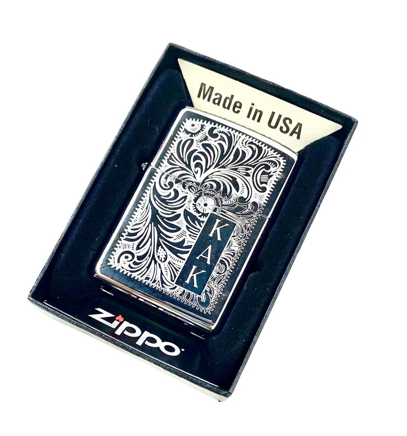 May include: Silver Zippo lighter with an engraved floral design and the initials "KAK" on the front. The lighter is in a black box with the words "Made in USA" and "Zippo" printed on it.
