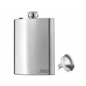 May include: A polished silver-tone metal flask with a curved rectangular body and a screw-top cap. The lower right corner features the engraved letters JHD. A small, matching silver-tone metal funnel is positioned to the right of the flask.