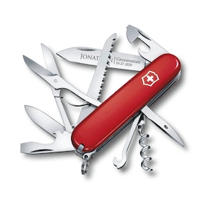 May include: A red Swiss Army Knife with a variety of tools, including a saw, a bottle opener, a corkscrew, a screwdriver, and a pair of scissors. The knife is engraved with the text "Groomsman 10-27-2020" and "JONAT".
