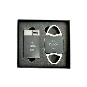 May include: A black gift box with a silver cigar cutter and lighter. The cutter and lighter are engraved with "#1 Daddy 2023".