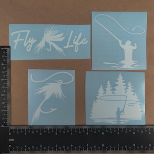 Puede incluir: Cuatro calcoman&iacute;as de vinilo blanco sobre un fondo azul claro. Las calcoman&iacute;as presentan temas de pesca con mosca. Una calcoman&iacute;a dice "Fly Life" con un se&ntilde;uelo de pesca con mosca. Otra calcoman&iacute;a muestra una silueta de un pescador con mosca lanzando una l&iacute;nea. La tercera calcoman&iacute;a muestra un se&ntilde;uelo de pesca con mosca con una l&iacute;nea. La cuarta calcoman&iacute;a muestra una silueta de un pescador con mosca lanzando una l&iacute;nea frente a una l&iacute;nea de pinos.