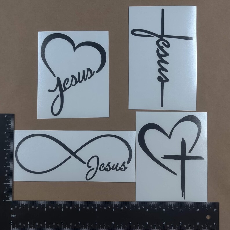 May include: Four black vinyl decals with different designs featuring the word "Jesus". The designs include a heart with the word "Jesus" inside, an infinity symbol with the word "Jesus" next to it, a cross with the word "Jesus" written vertically, and a heart with a cross inside.