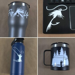 Puede incluir: Cuatro art&iacute;culos diferentes con un tema de pesca con mosca. Un vaso gris con el texto "Fly Life" y un dise&ntilde;o de se&ntilde;uelo de pesca con mosca. Un port&aacute;til negro con un dise&ntilde;o de se&ntilde;uelo de pesca con mosca blanco. Una botella de agua azul con una silueta blanca de una persona pescando con mosca. Una taza negra con una silueta blanca de una persona pescando con mosca en un entorno de bosque.