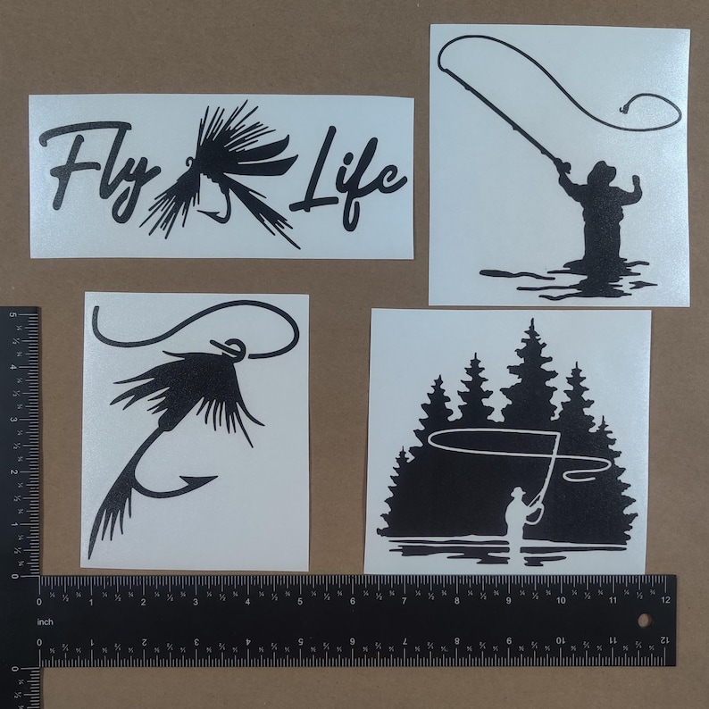 Puede incluir: Cuatro calcoman&iacute;as de vinilo en blanco y negro con tem&aacute;tica de pesca con mosca. La primera calcoman&iacute;a dice "Fly Life" con un se&ntilde;uelo de pesca con mosca. La segunda calcoman&iacute;a muestra una silueta de una persona pescando con mosca. La tercera calcoman&iacute;a muestra un se&ntilde;uelo de pesca con mosca. La cuarta calcoman&iacute;a muestra una silueta de una persona pescando con mosca frente a un bosque.
