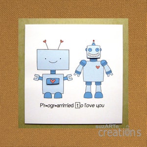 May include: A card with two blue robots holding hands. The robot on the left has a heart on its chest and the robot on the right has a heart on its torso. The card says "Programmed to love you".
