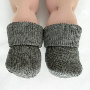 May include: A pair of charcoal gray knit socks with a ribbed texture and a folded cuff. The socks are made from a soft, heathered material and feature a simple, rounded toe design. The fabric has a visible knit pattern throughout the entire garment.