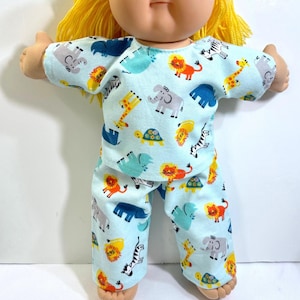 May include: A doll with bright yellow yarn hair wearing a light blue short-sleeved shirt and matching pants. The fabric features a repeating pattern of colorful cartoon animals including lions, elephants, giraffes, zebras, and turtles.