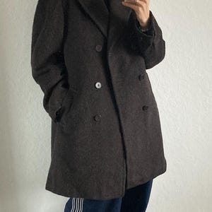 May include: A dark brown double-breasted coat with large buttons. The coat is worn with a black turtleneck, blue sweatpants with white stripes, and red sneakers with white stripes.